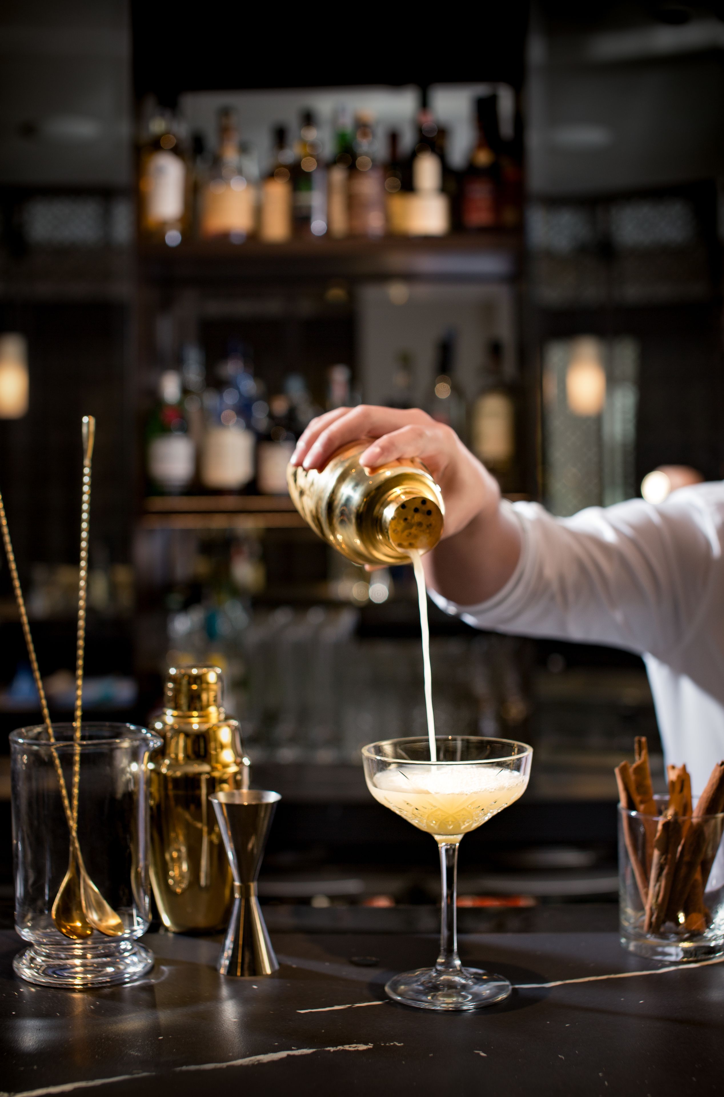 A bartender pouring a drink into a martini glass.