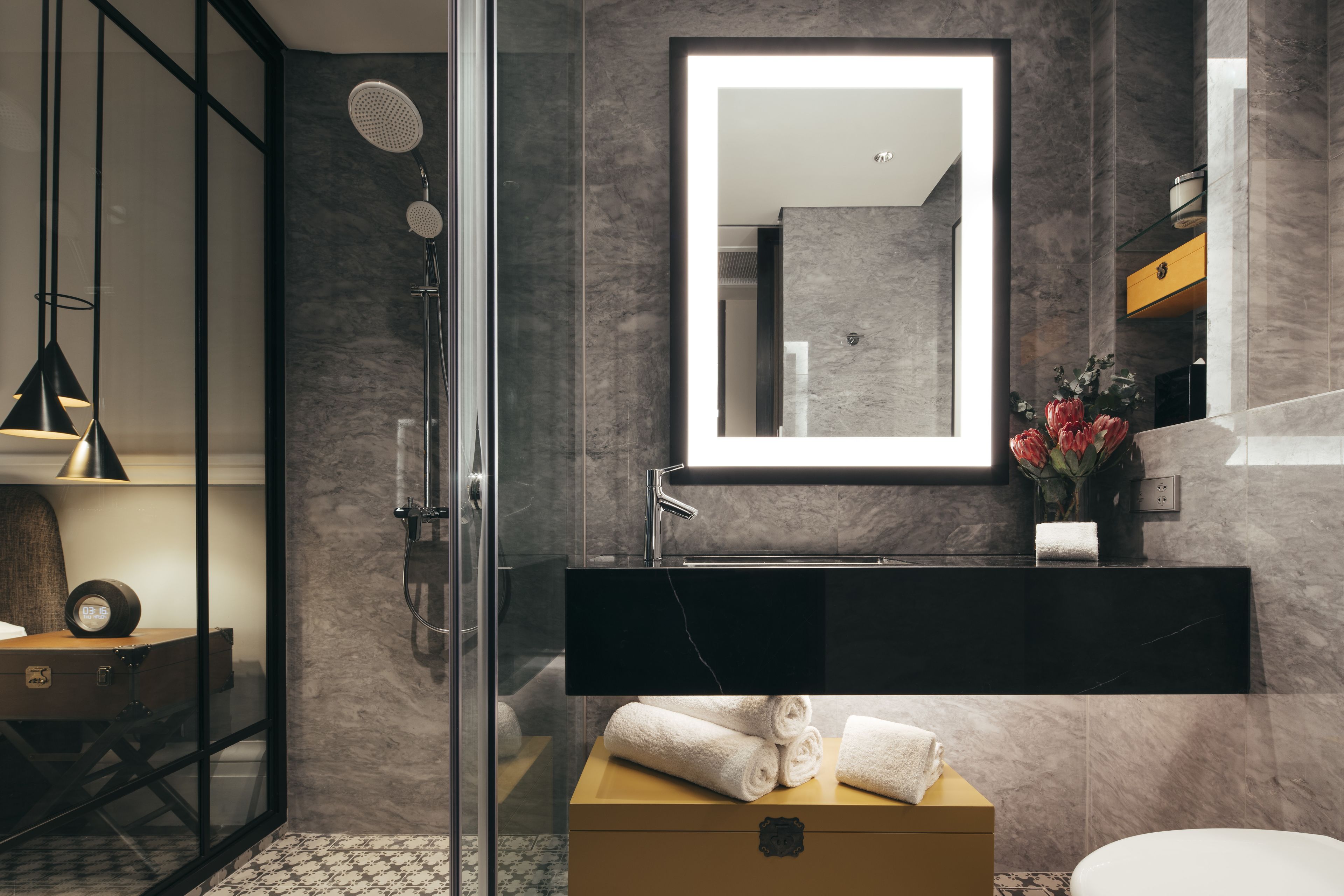 A modern bathroom with a glass-enclosed shower, a black vanity, and a marble-tiled wall.