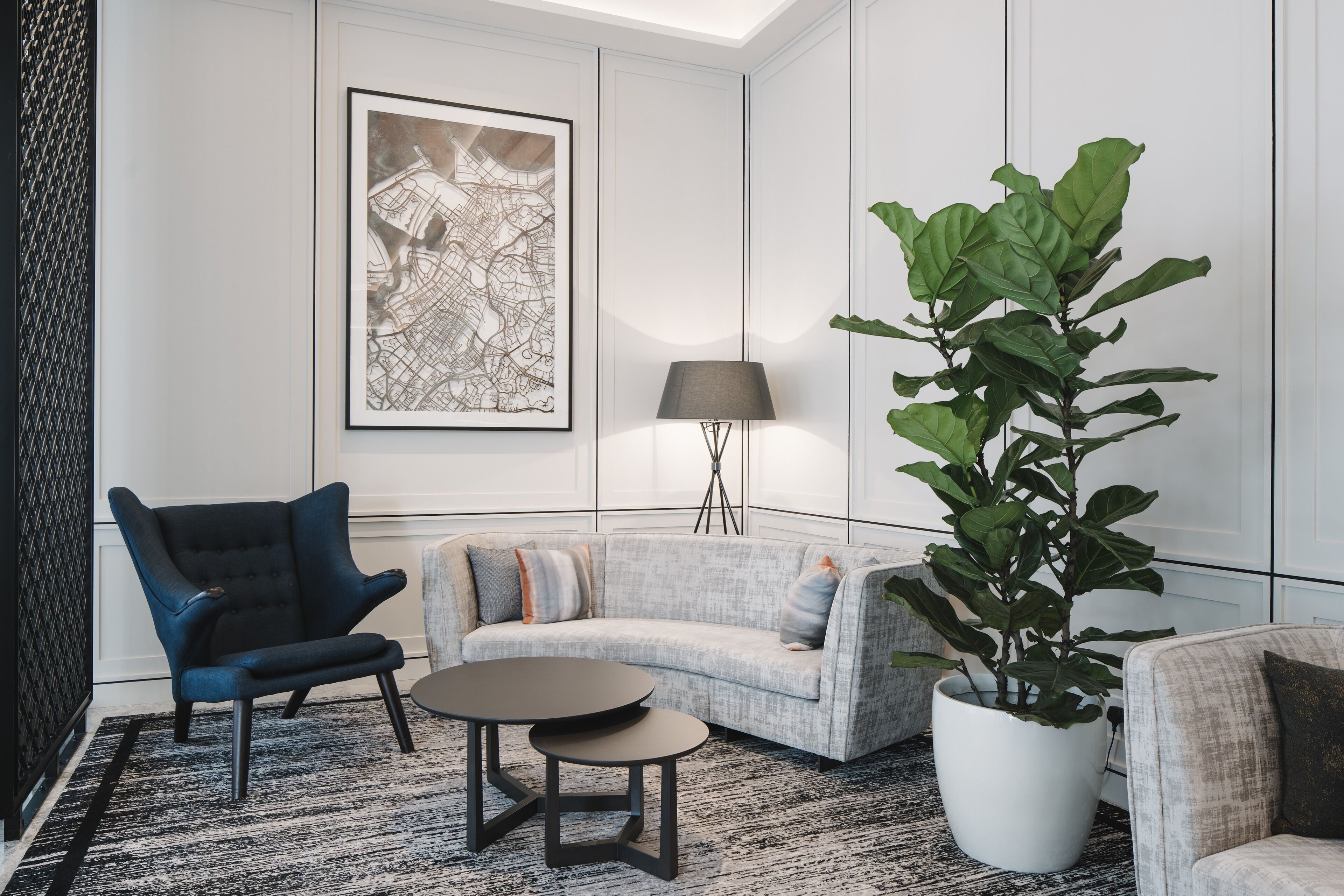 A modern living room with a sectional sofa, a dark armchair, a small round table, a floor lamp, and a large potted plant.