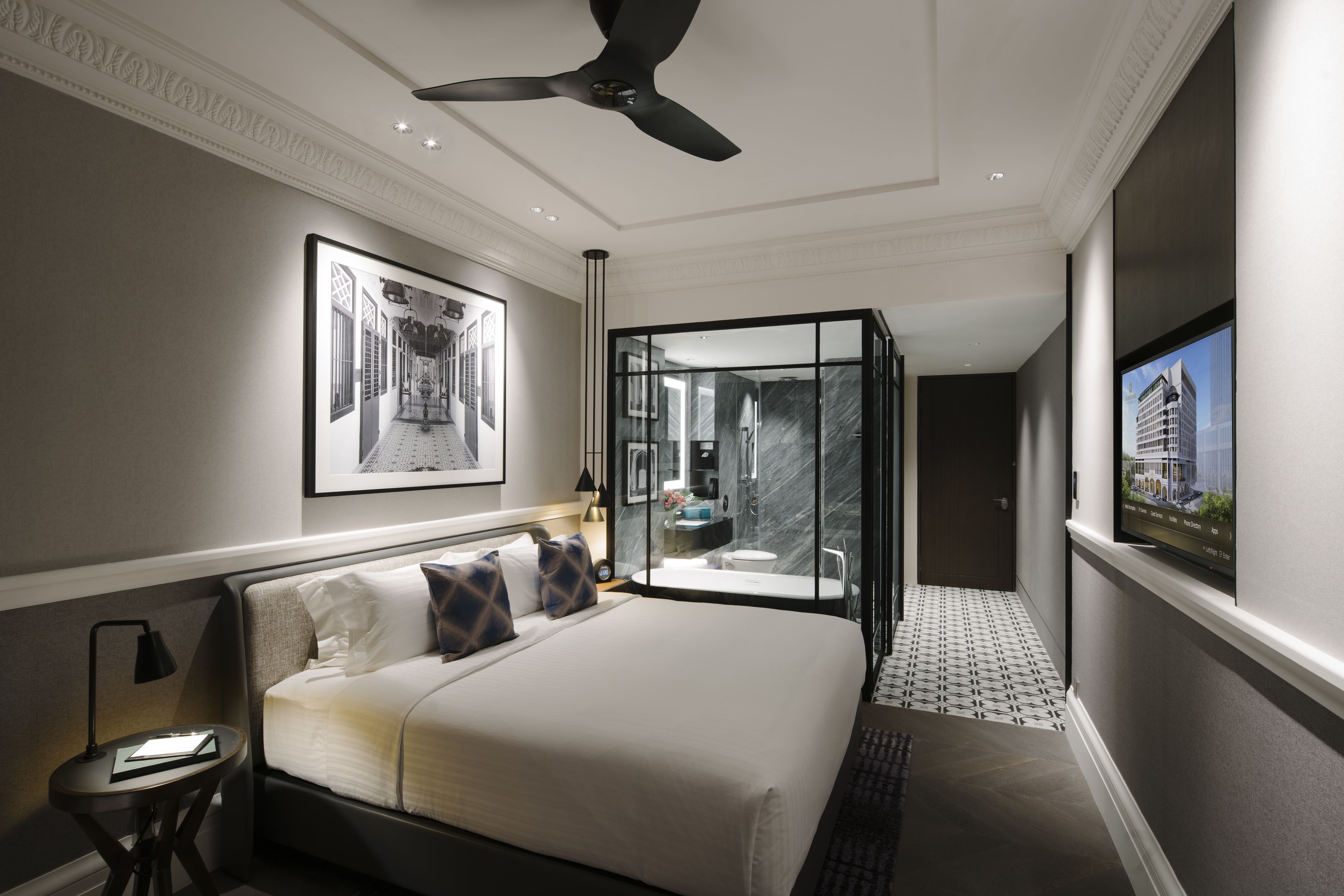 A modern hotel room with a large bed, a glass-enclosed bathroom, and a view of a cityscape.