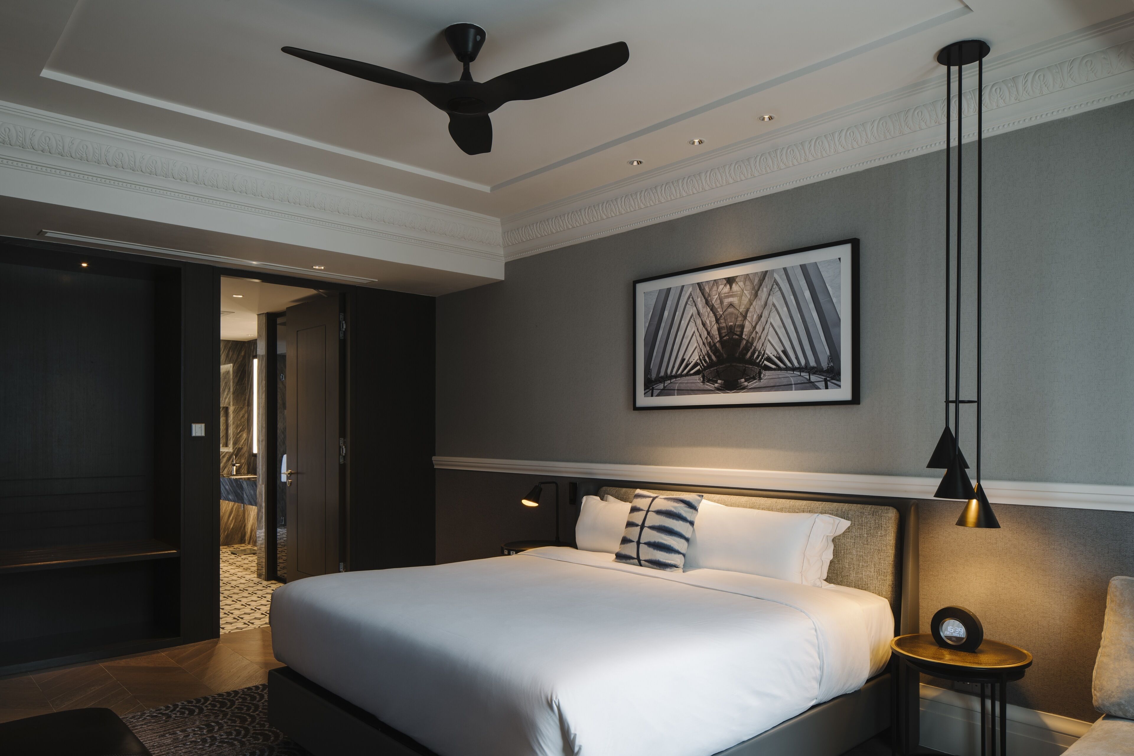 Une chambre d’hôtel moderne avec un grand lit, un ventilateur de plafond, une œuvre d’art encadrée et une table de chevet avec une lampe.