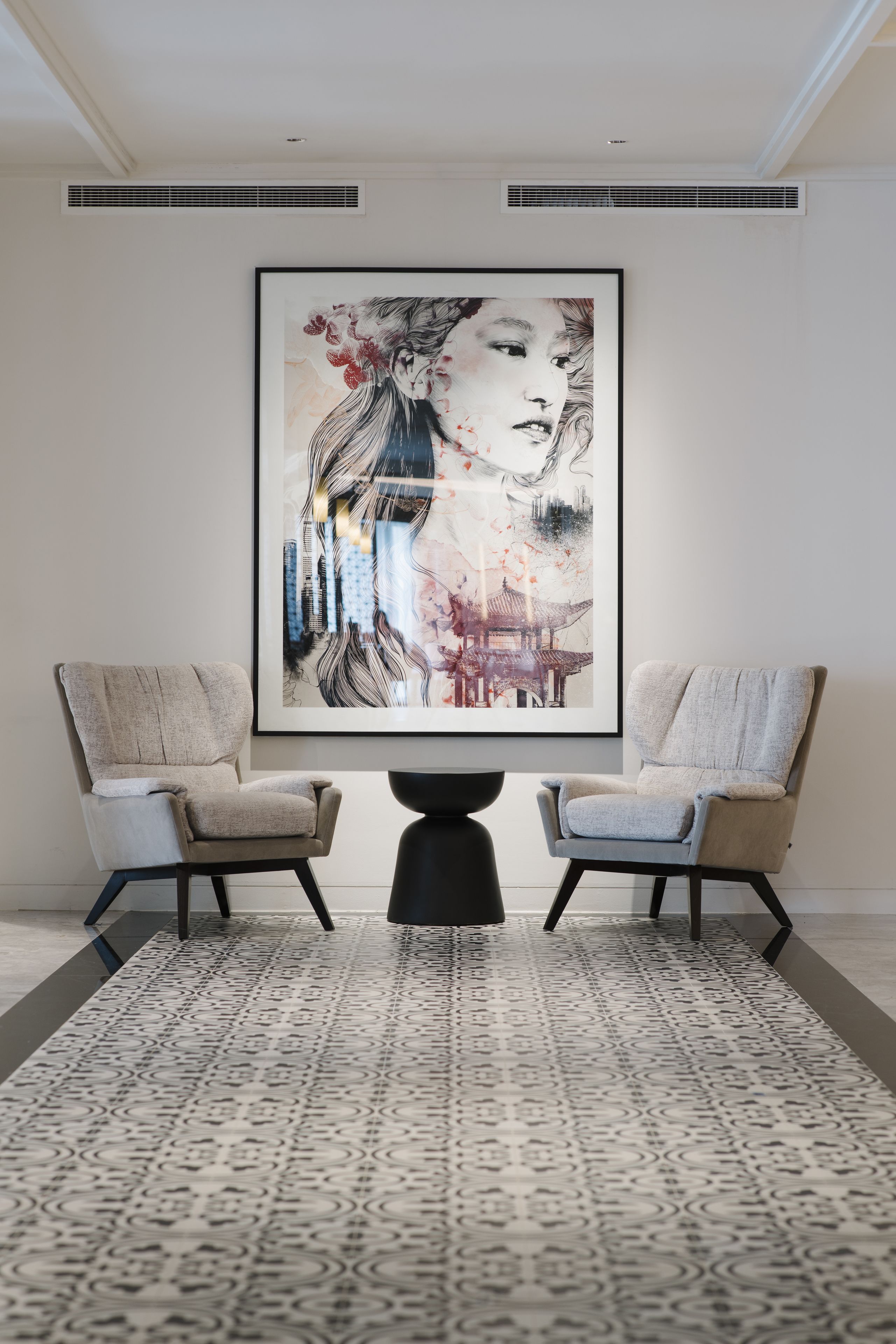 A modern room with two armchairs, a patterned rug, and a large framed artwork on the wall.