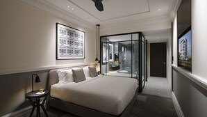 Una habitación de hotel moderna con una cama grande, un ventilador de techo, un cuadro enmarcado en la pared y un baño con paredes de vidrio.