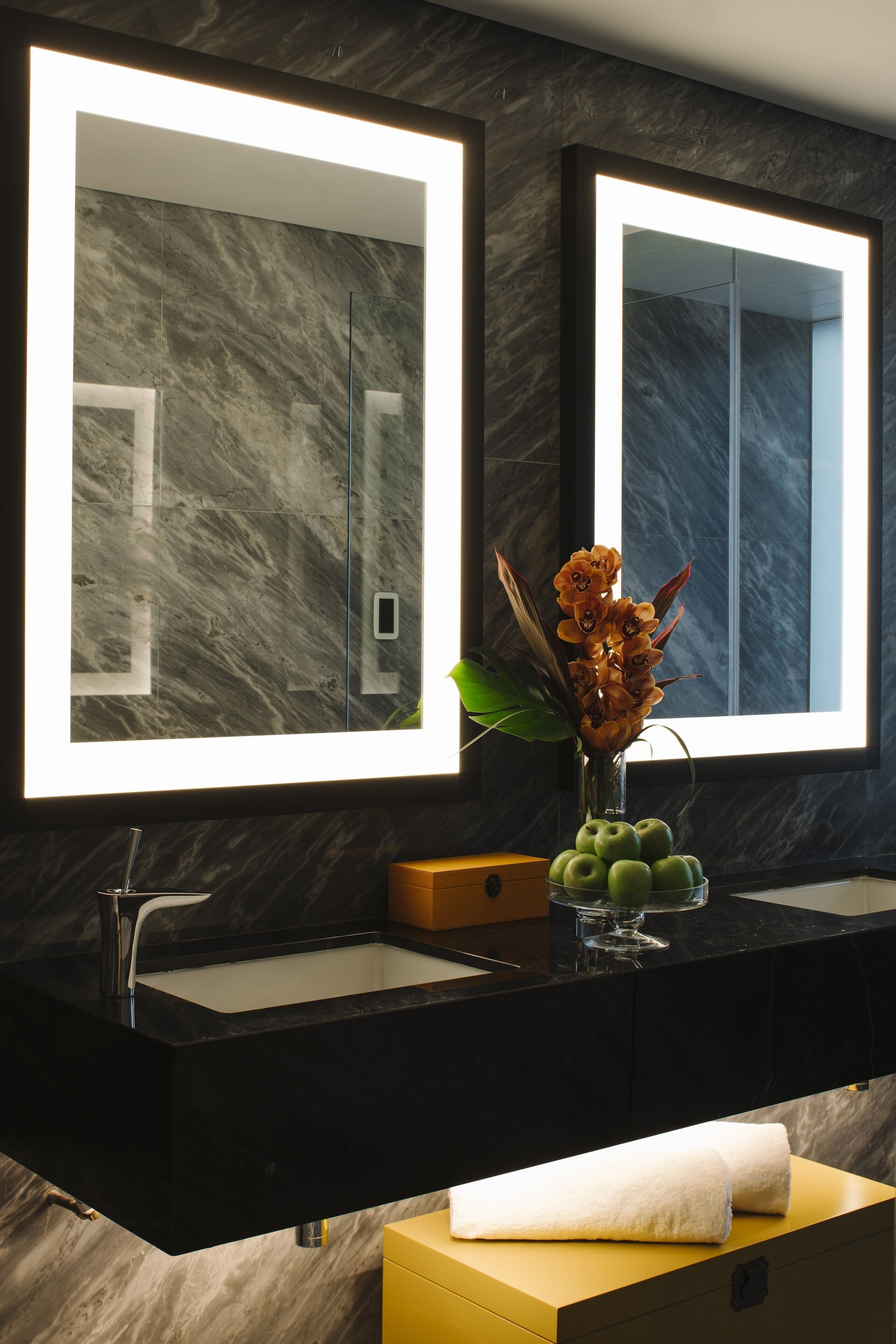A modern bathroom with two mirrors, a black sink, and a vase with flowers.