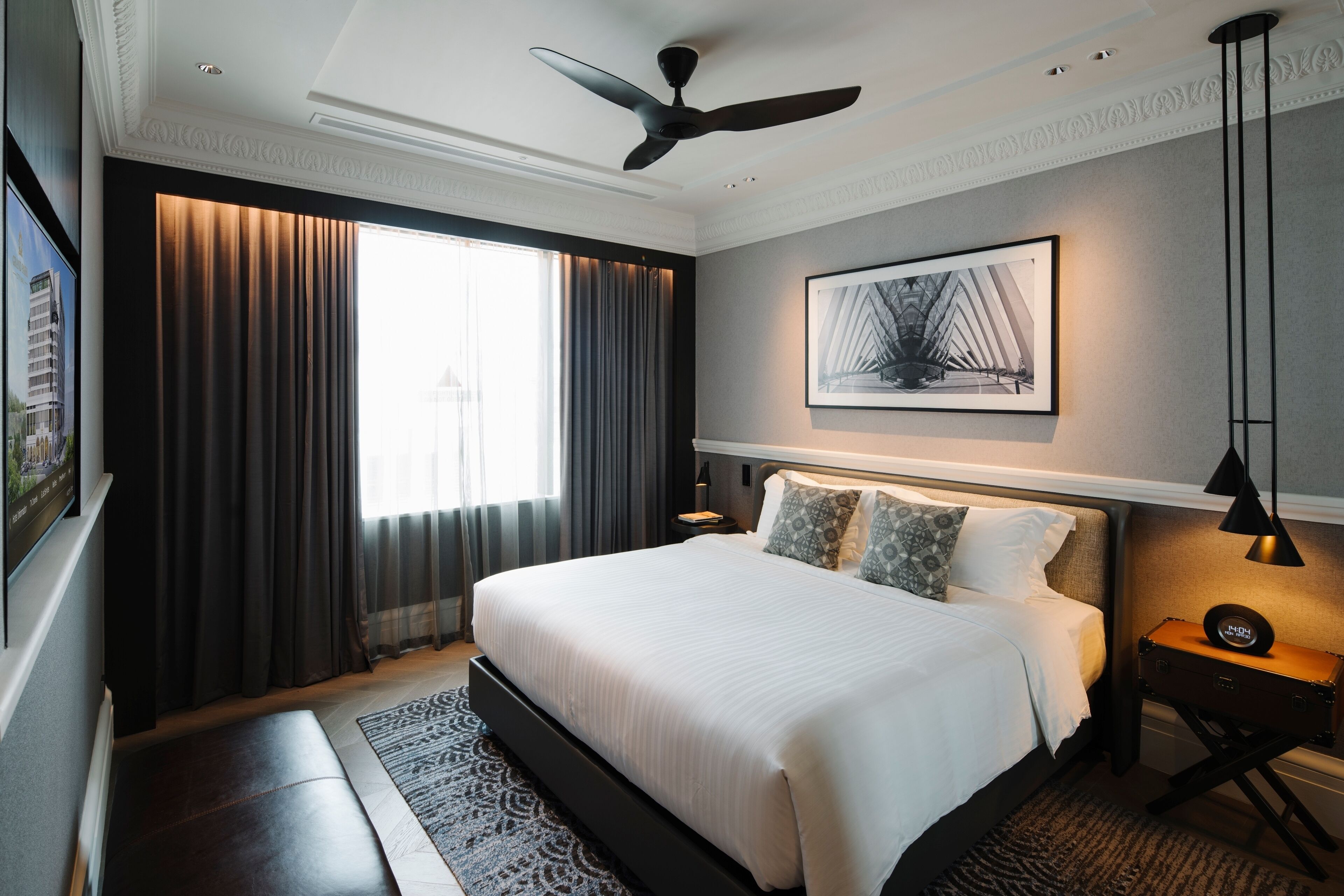 Una habitación de hotel moderna con una cama grande, un ventilador de techo, un cuadro enmarcado en la pared y una mesita de noche con una lámpara.
