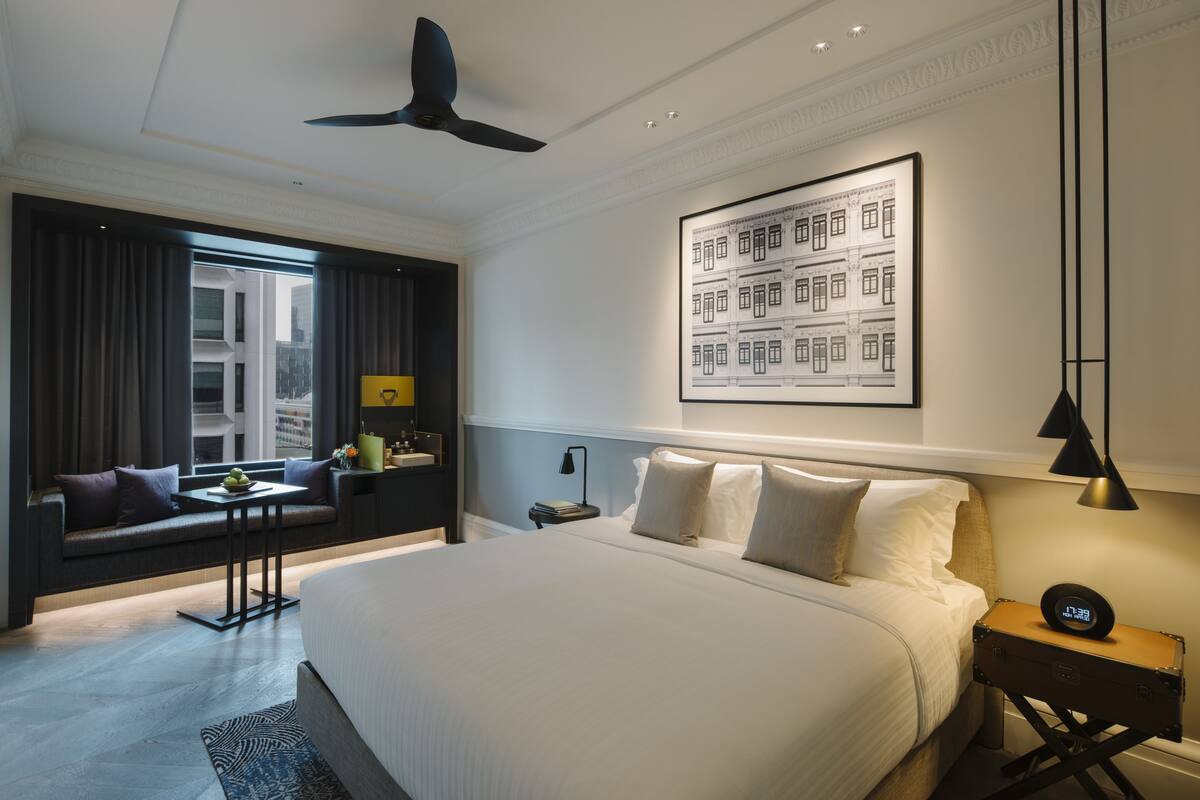 A modern hotel room with a large bed, a sofa, a desk, and a ceiling fan.