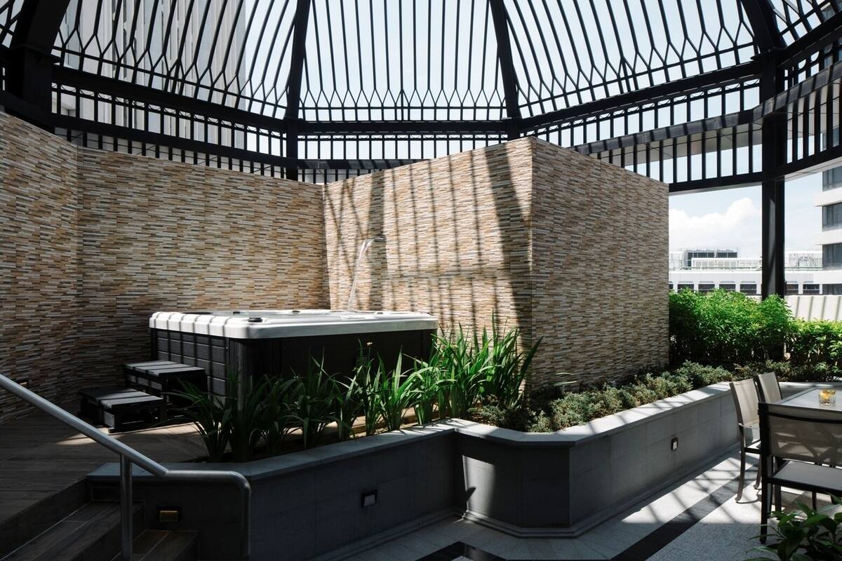 A modern outdoor lounge area with a geometric metal roof, stone walls, and a central seating area with a hot tub.