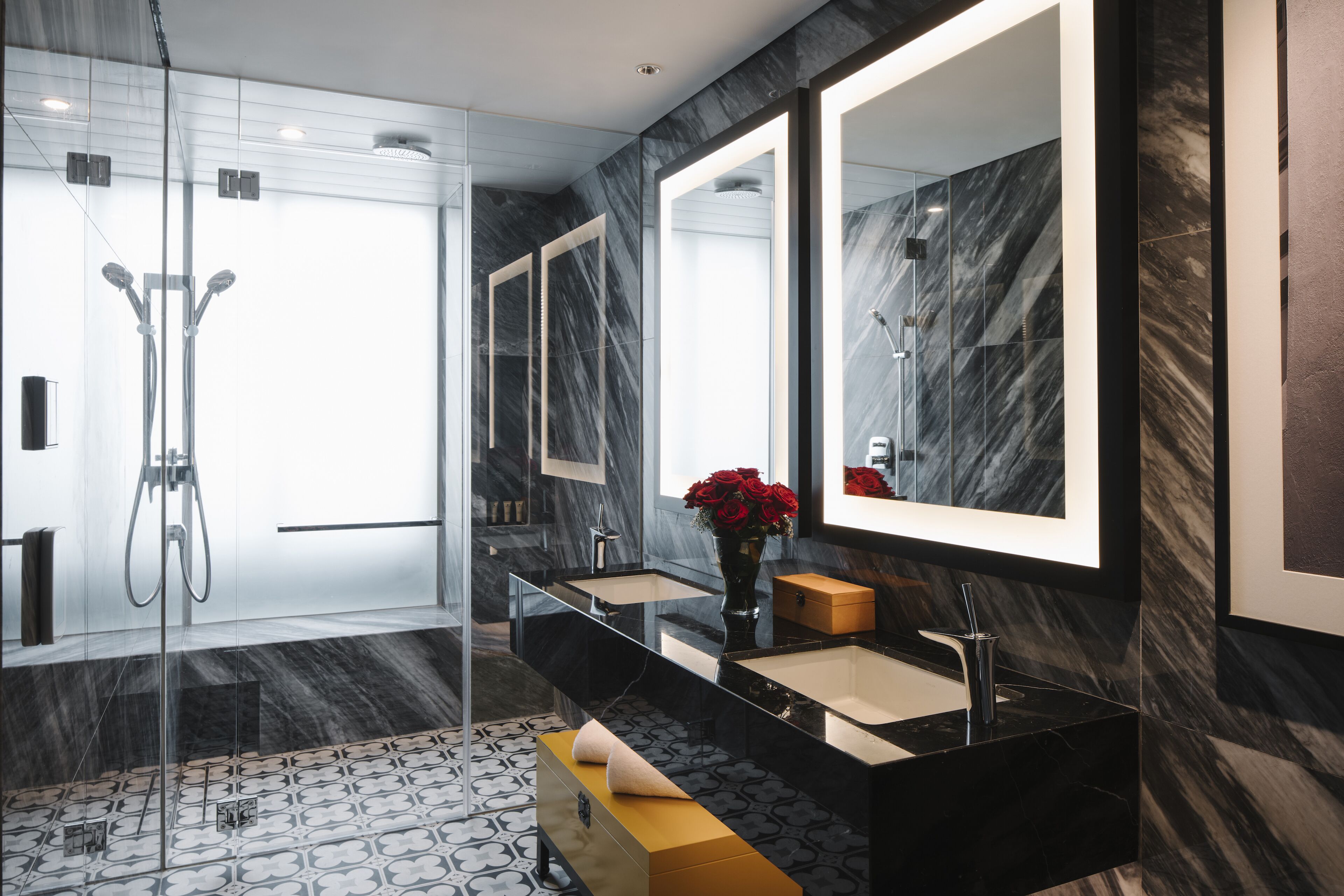 A modern bathroom with a glass-enclosed shower, a black marble vanity, and a large mirror.