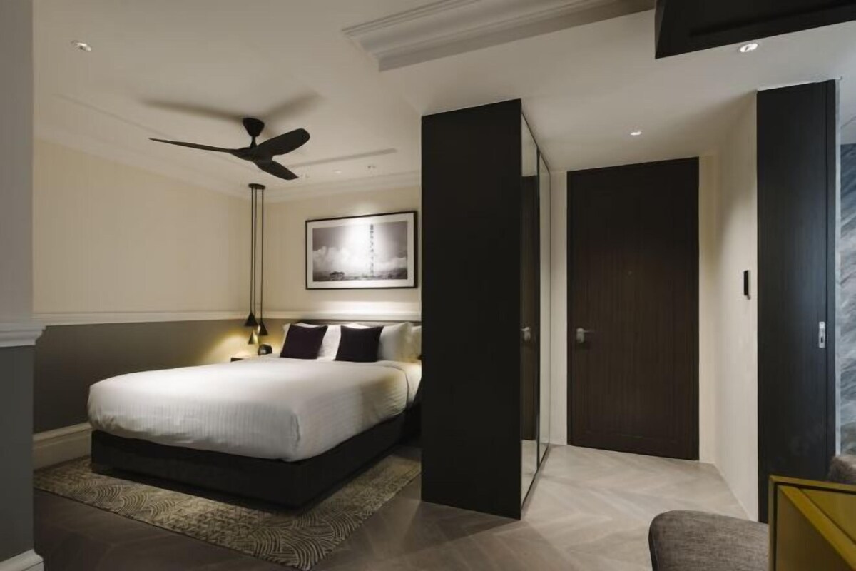 A modern bedroom with a bed, a ceiling fan, a nightstand, a framed picture on the wall, and a door.