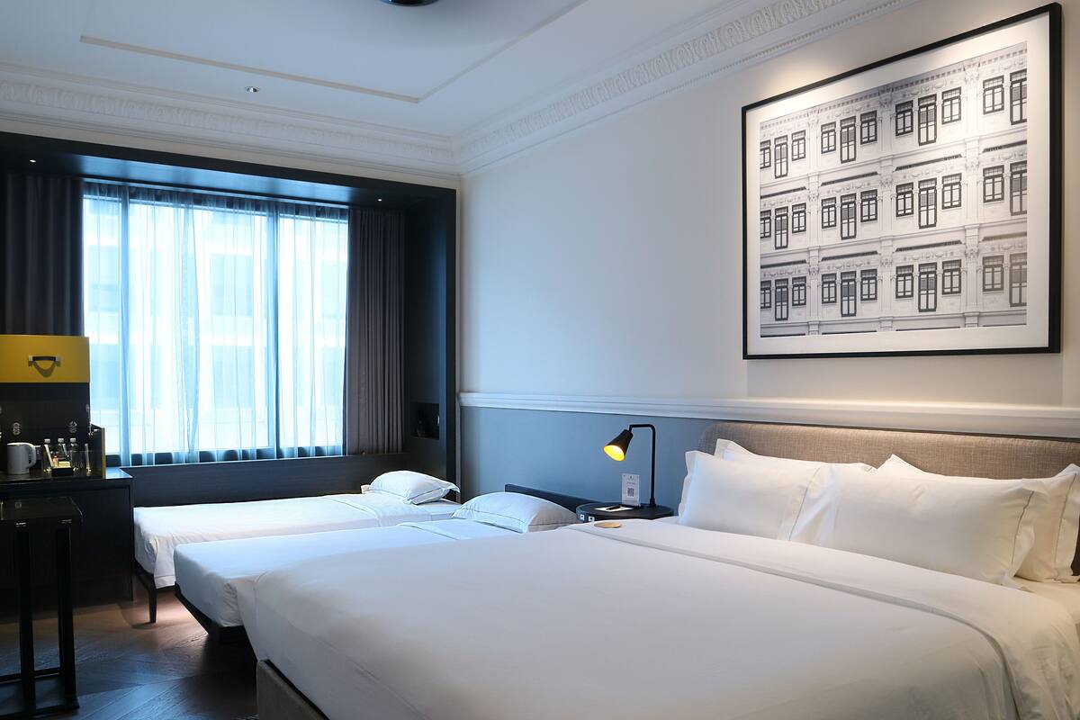 A hotel room with two beds, a desk, a lamp, and a large framed picture on the wall.