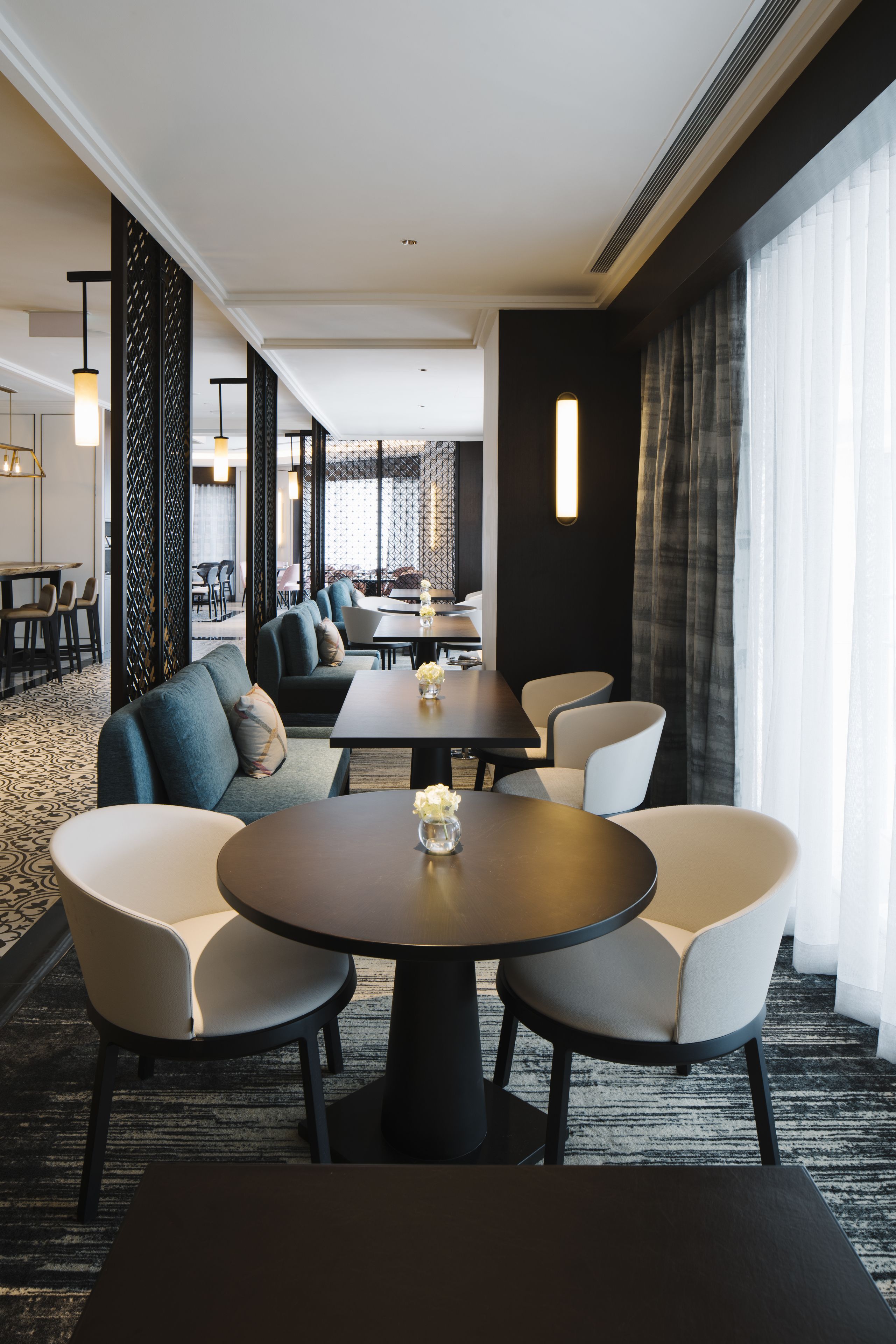 A modern hotel lobby with a central seating area, a bar, and a view of the cityscape through large windows.
