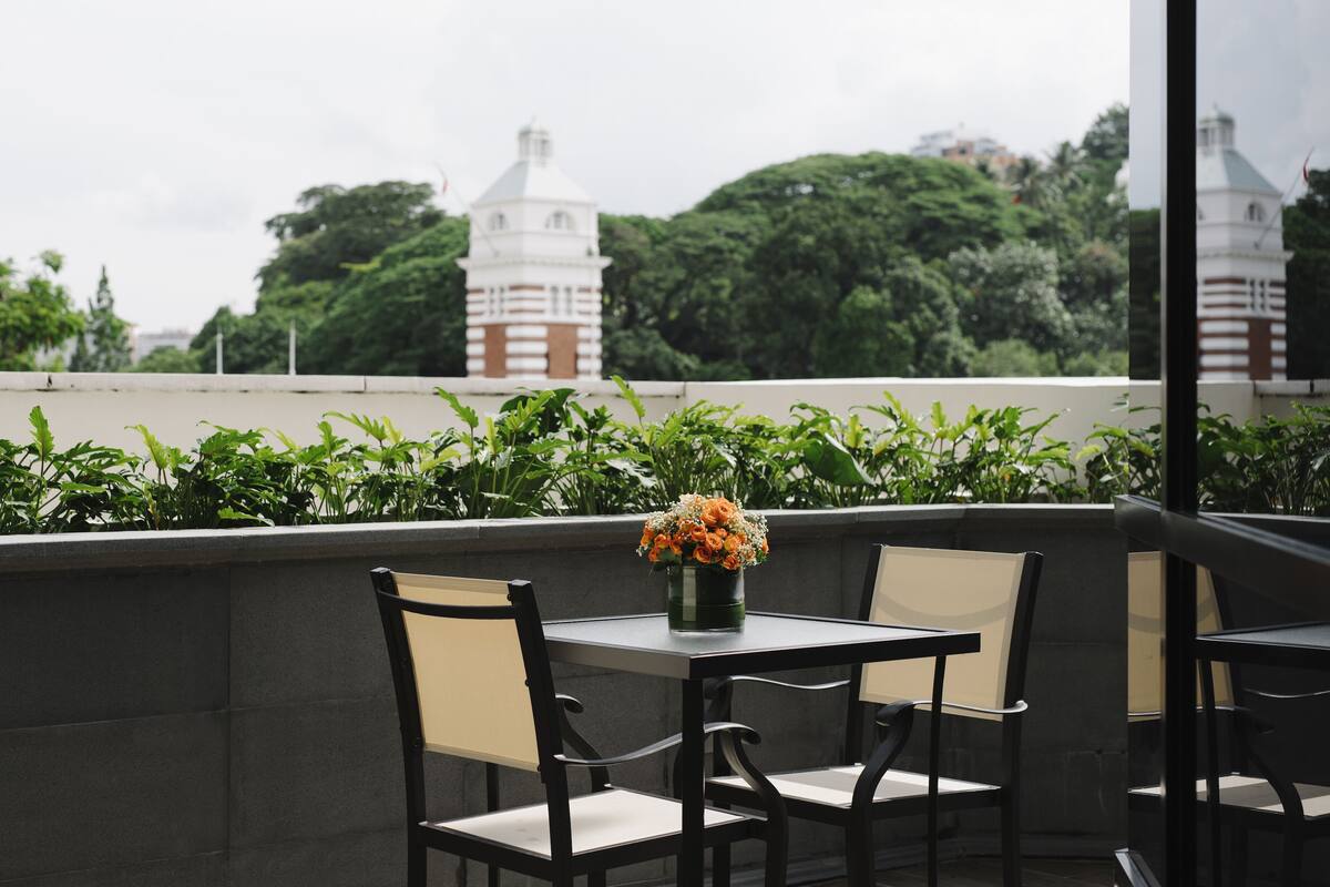 A terrace with a table and chairs, a vase with flowers, and a view of a tower and trees.