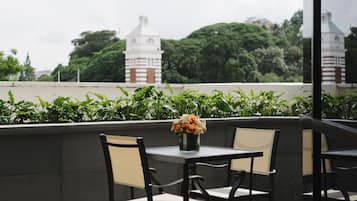 Una terraza con mesa y sillas, un florero con flores y vistas a una torre y árboles.