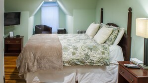 A bedroom with a bed, a bedside table, a chair, a TV, and a window. - Beacon Inn 1750 (Brookline)