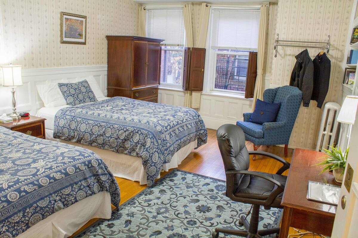 Habitación de hotel con dos camas, una silla, un escritorio y una ventana con cortinas.