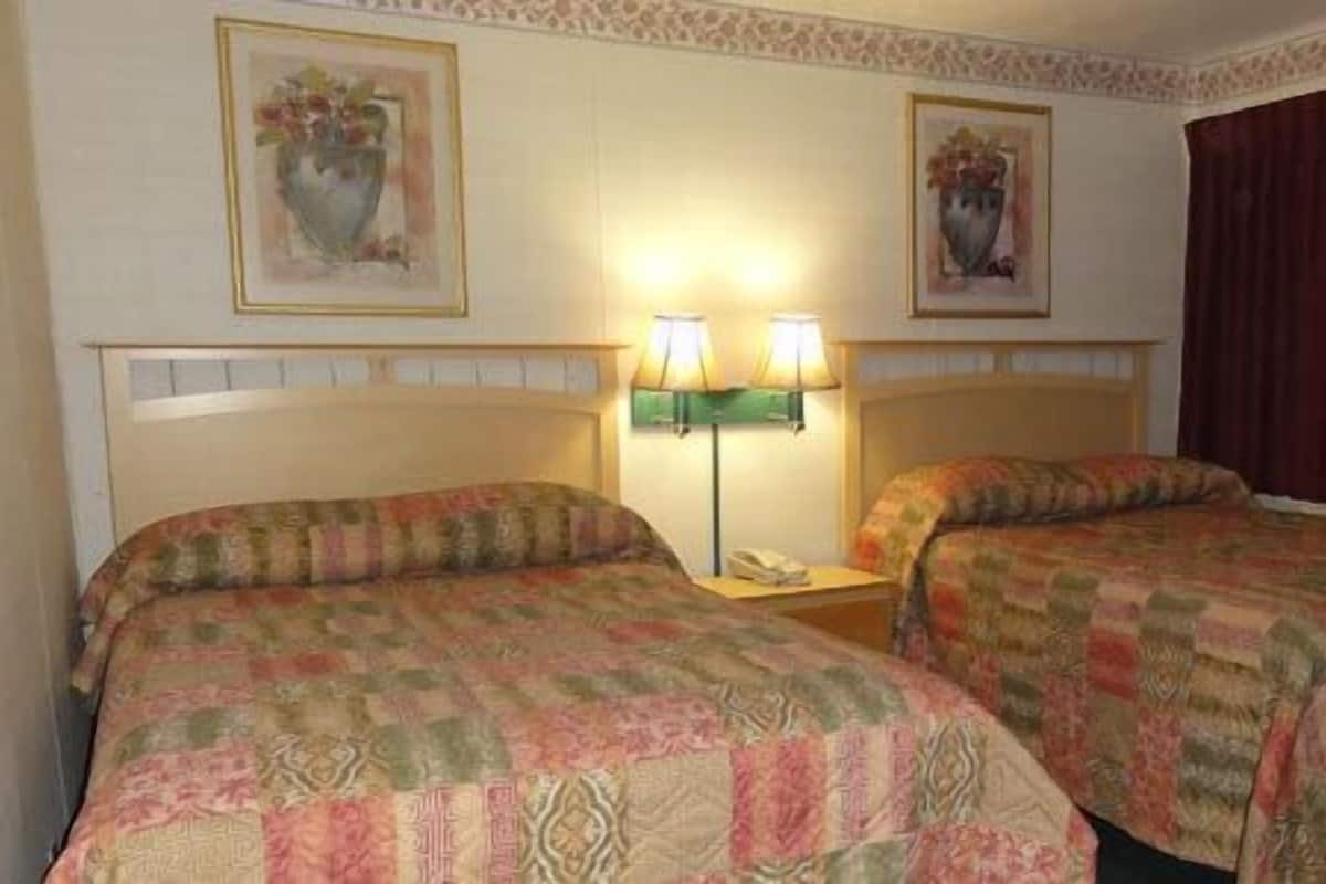 A hotel room with two beds, a nightstand, and two wall-mounted lamps.