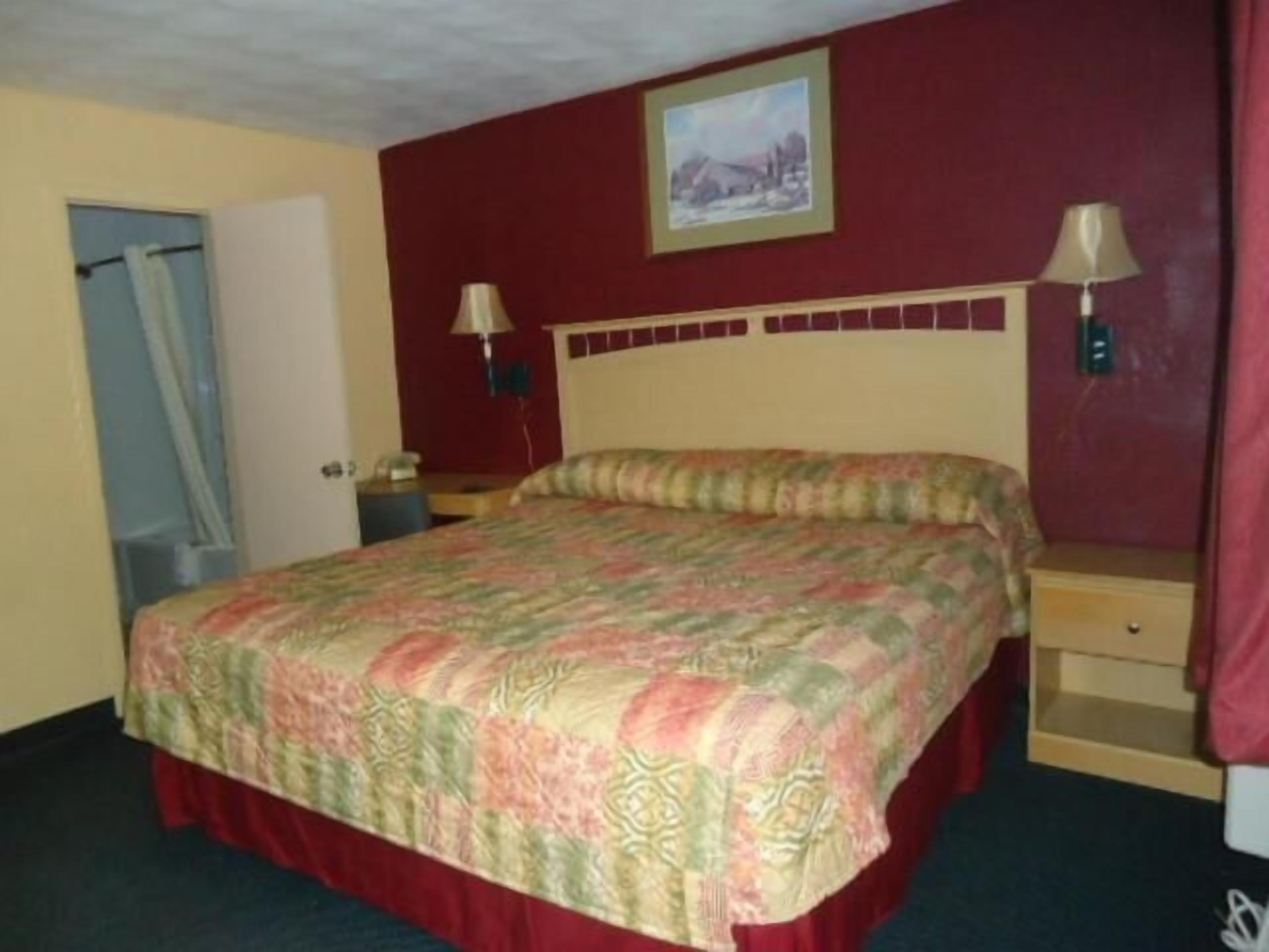A hotel room with a bed, two bedside tables, a nightstand, a lamp, and a painting on the wall.