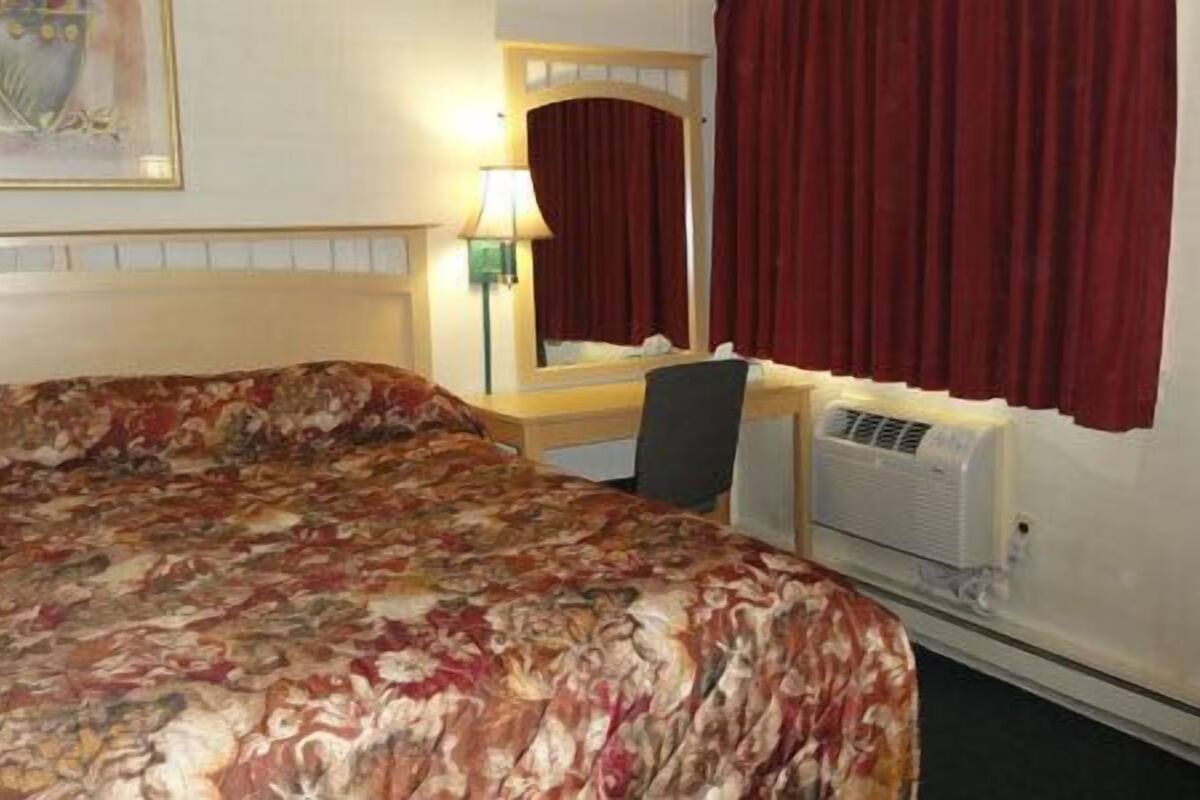 A hotel room with a bed, a desk, a mirror, and a window with curtains.
