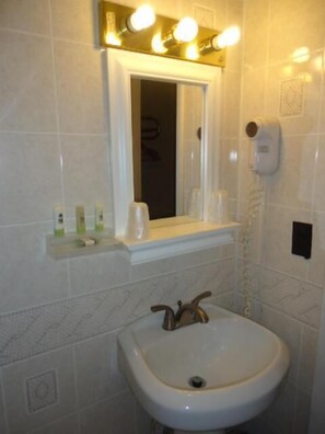Une salle de bain équipée d’un lavabo, d’un miroir et d’une étagère où sont rangés les articles de toilette.