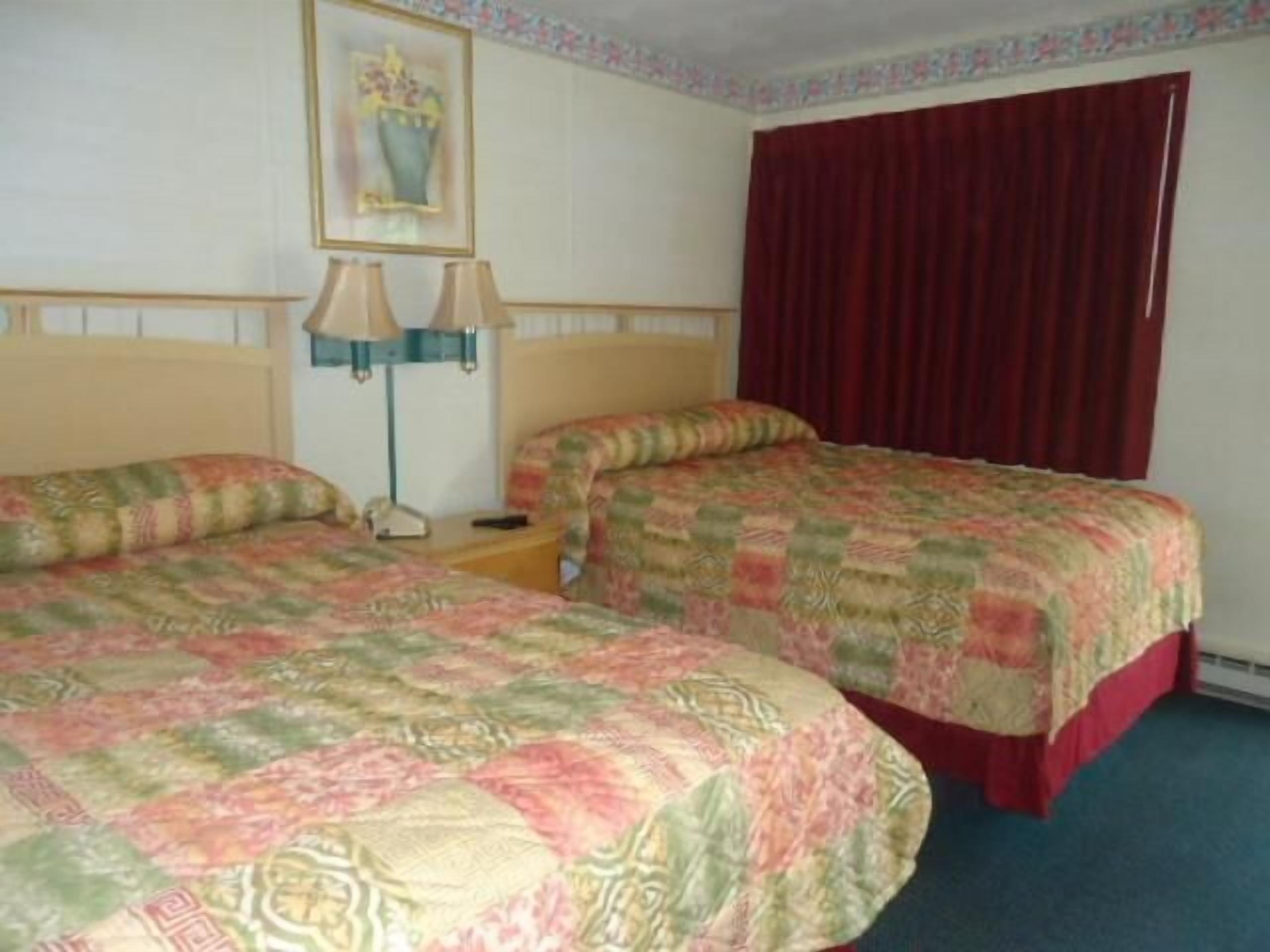 Camera d'albergo con due letti, un comodino, una lampada, un quadro e una finestra con tende.