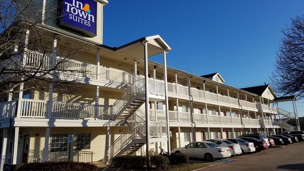Un motel de varios pisos con un letrero llamativo que dice "Inn Town Suites". Tiene un estacionamiento con varios coches, múltiples balcones y una escalera que conecta los pisos.