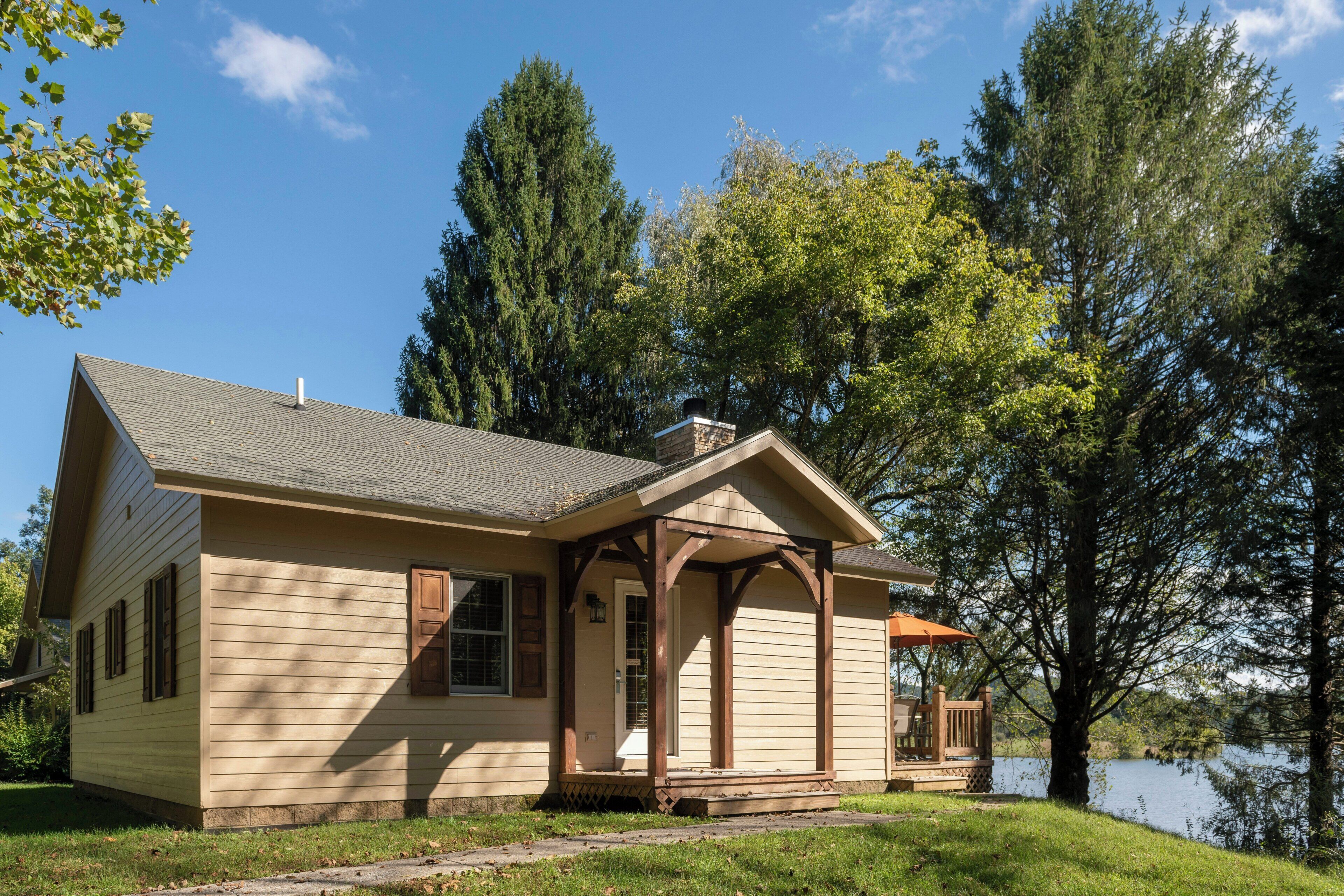 A single-story house with a gabled roof, a front porch with wooden columns, and a small deck with outdoor furniture.