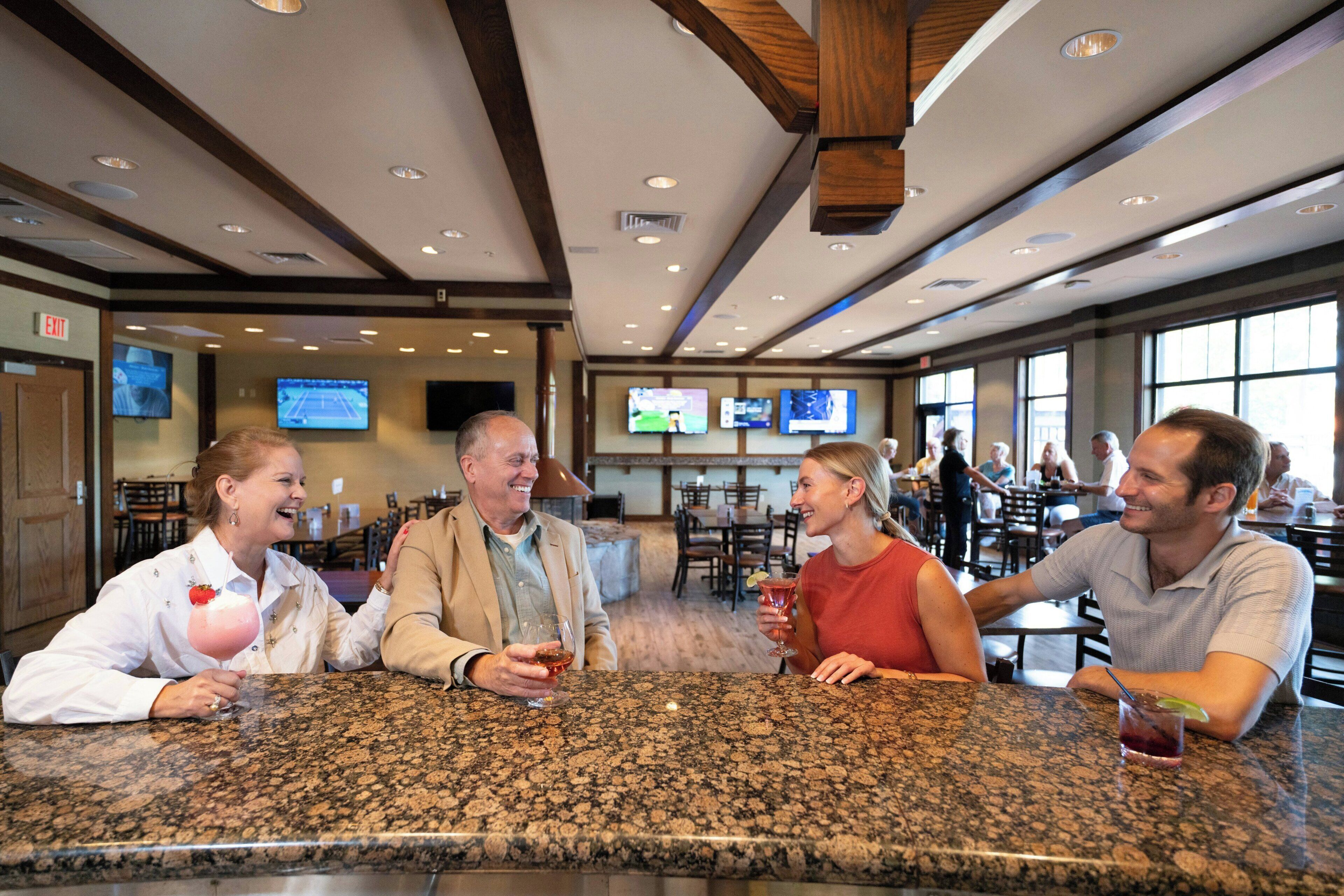 A bar area with granite countertops, multiple screens displaying sports, and a high ceiling with wooden beams.
