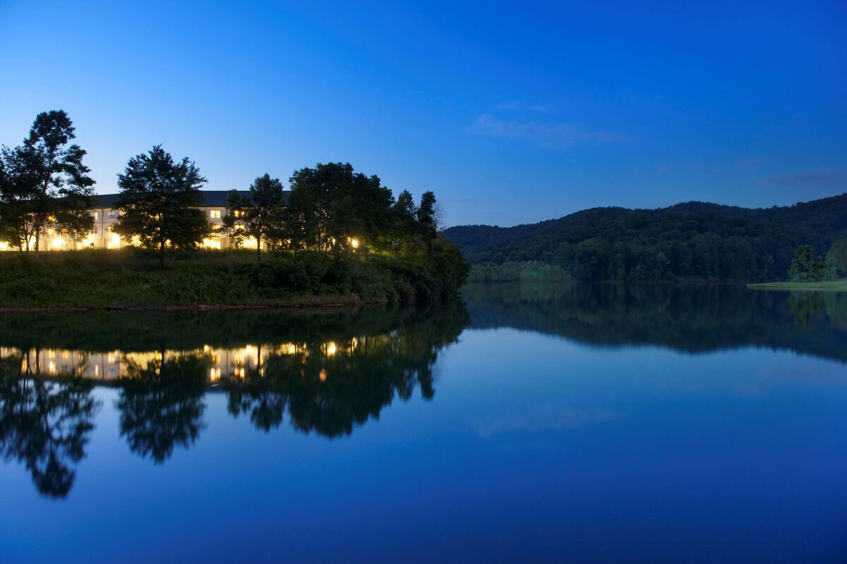 Vista de un edificio junto al lago, con árboles y su reflejo en el agua.
