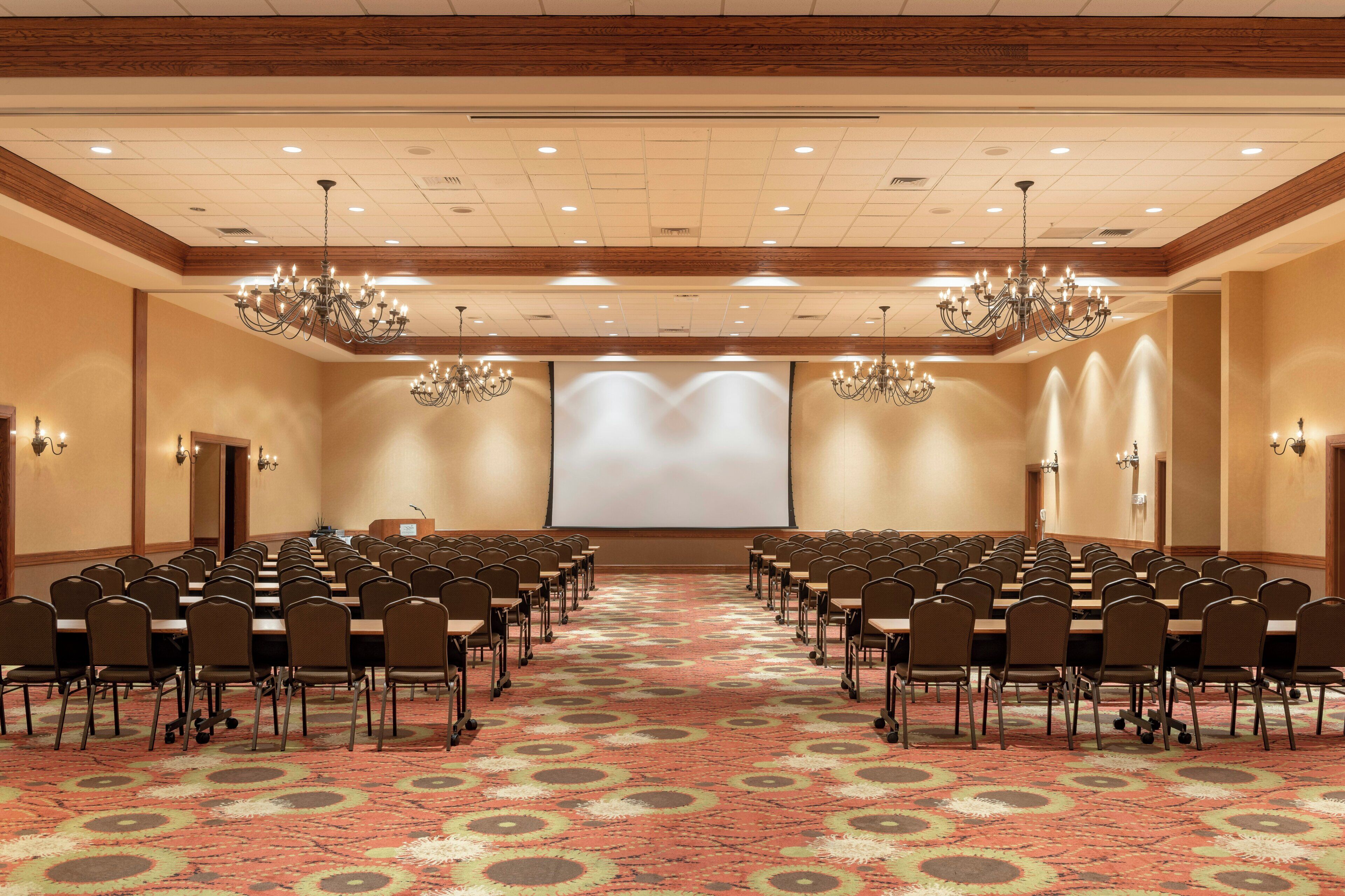 A conference room with rows of chairs, a projector screen, and chandeliers.