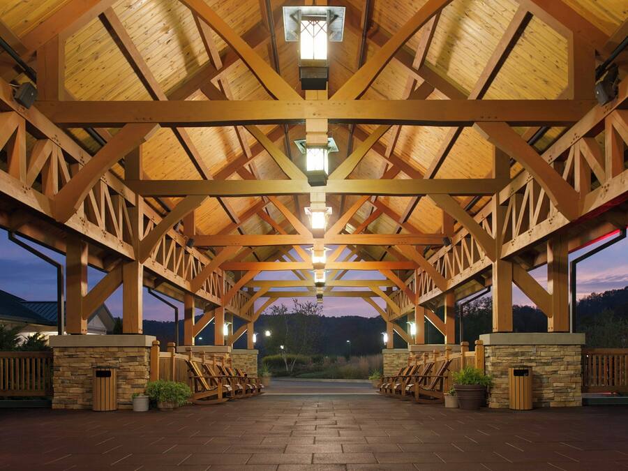 Un espacio al aire libre techado con estructura de madera, paredes de piedra y disposición de asientos.