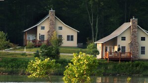 Two houses with stone chimneys, wooden decks, and a pond in the foreground. - Stonewall Resort (Roanoke)