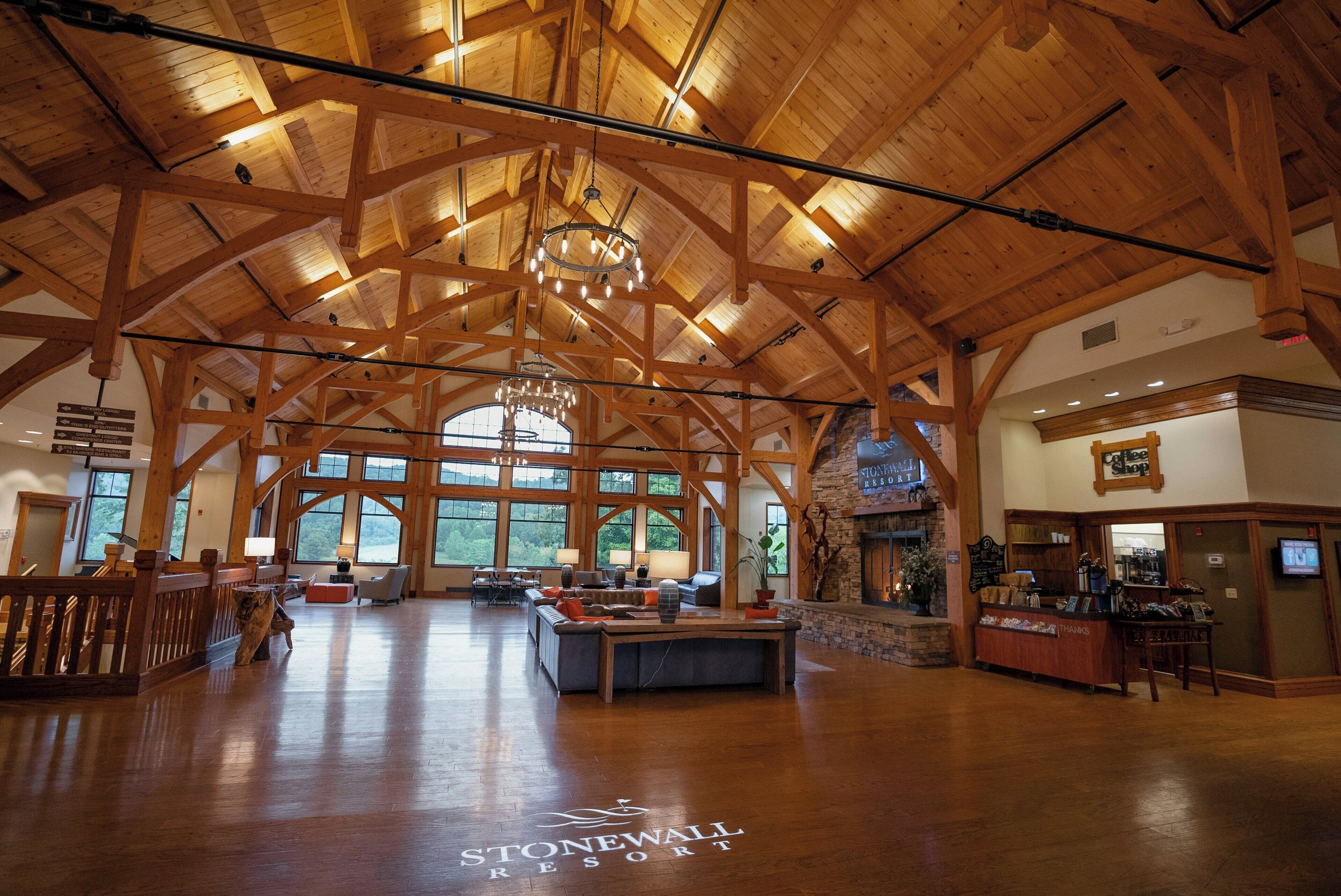 Un intérieur spacieux avec de hauts plafonds en bois, un espace salon central et de grandes fenêtres offrant une vue sur l’extérieur.