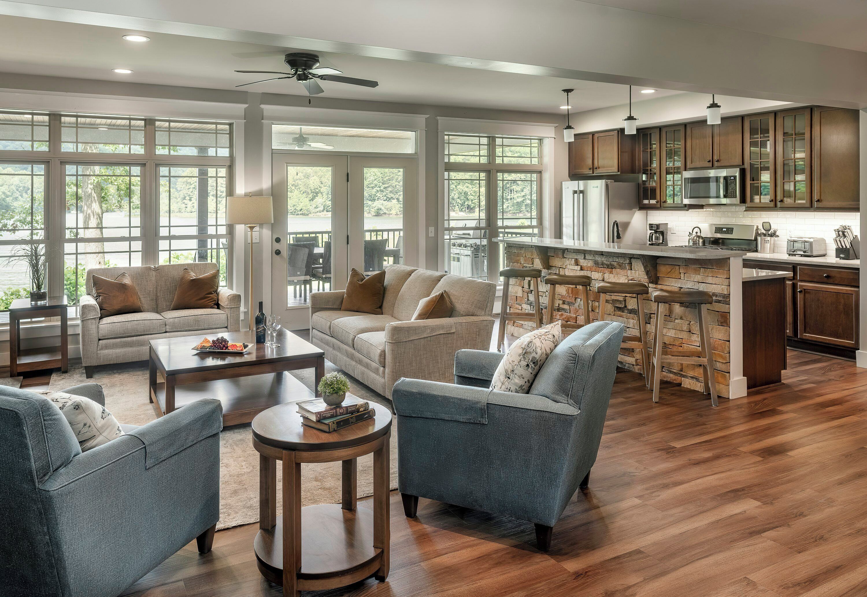 A spacious living room with a large window, a ceiling fan, and a kitchen area with a stone island and bar stools.