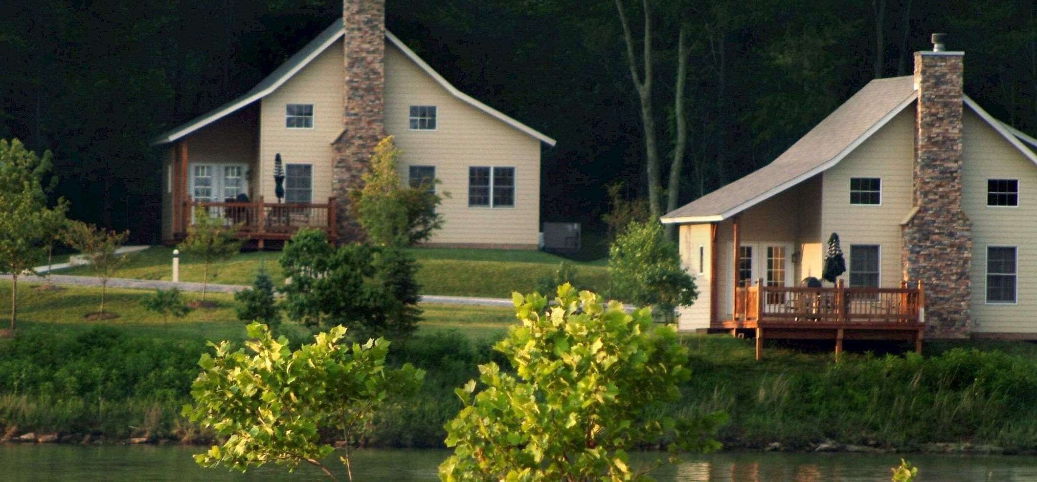 Two houses with stone chimneys, a wooden deck, and a grassy area with trees.