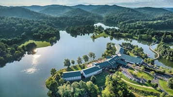 A large building with a green roof, surrounded by a lake and forested hills.