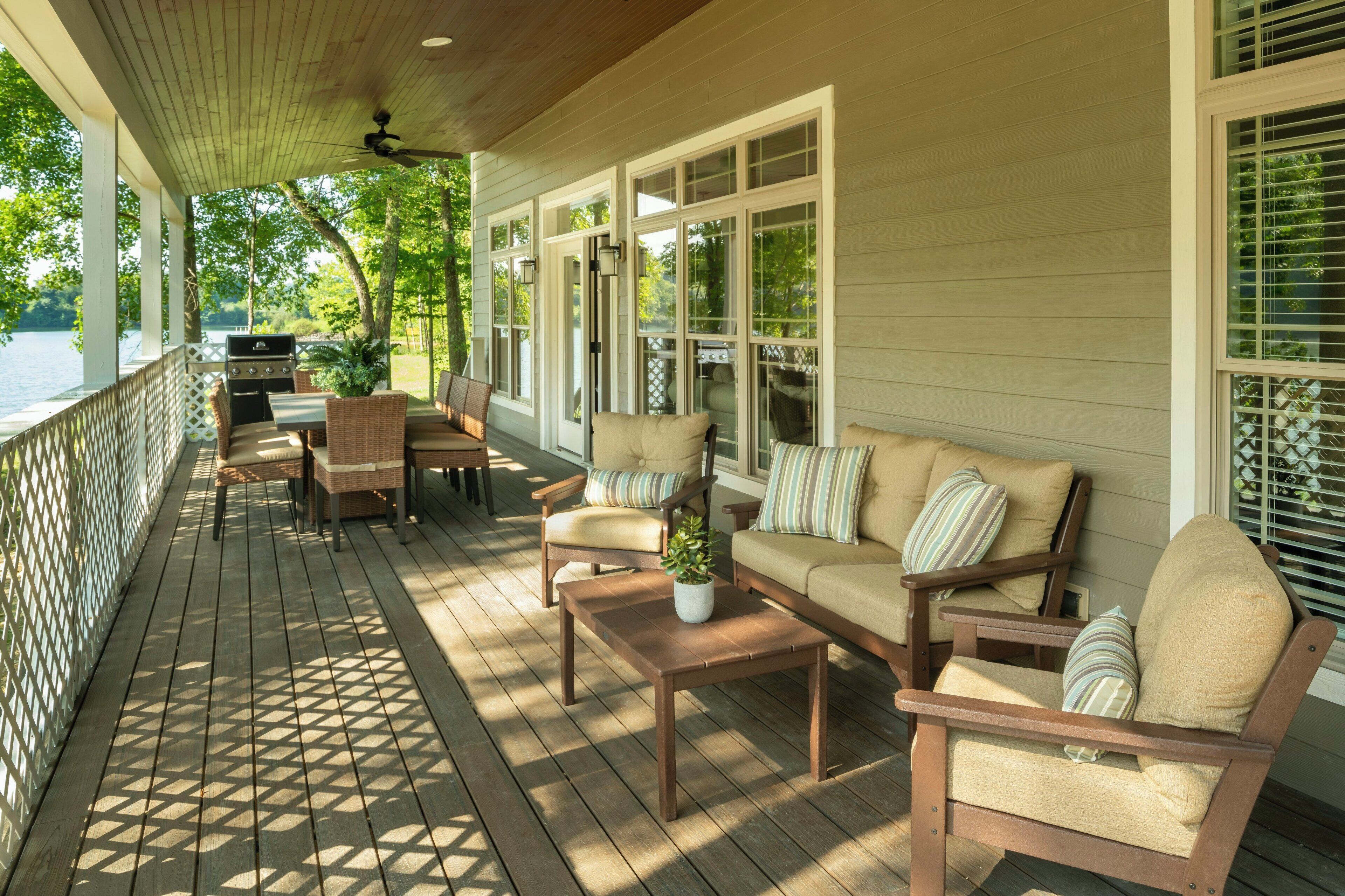 Eine überdachte Veranda mit Gartenmöbeln, einem Grill und großen Fenstern.