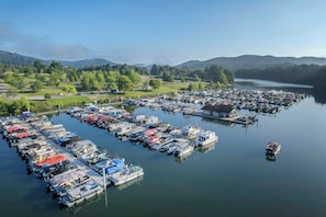 Un port de plaisance où sont amarrés de nombreux bateaux, entouré d’un paysage vallonné et bordé d’un lac paisible.