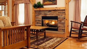 A cozy living room with a stone fireplace, wooden beams, a sofa, a table, and a rocking chair. - Stonewall Resort (Roanoke)