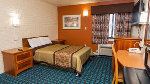 A hotel room with a bed, a desk, a chair, a TV, and a window with curtains.