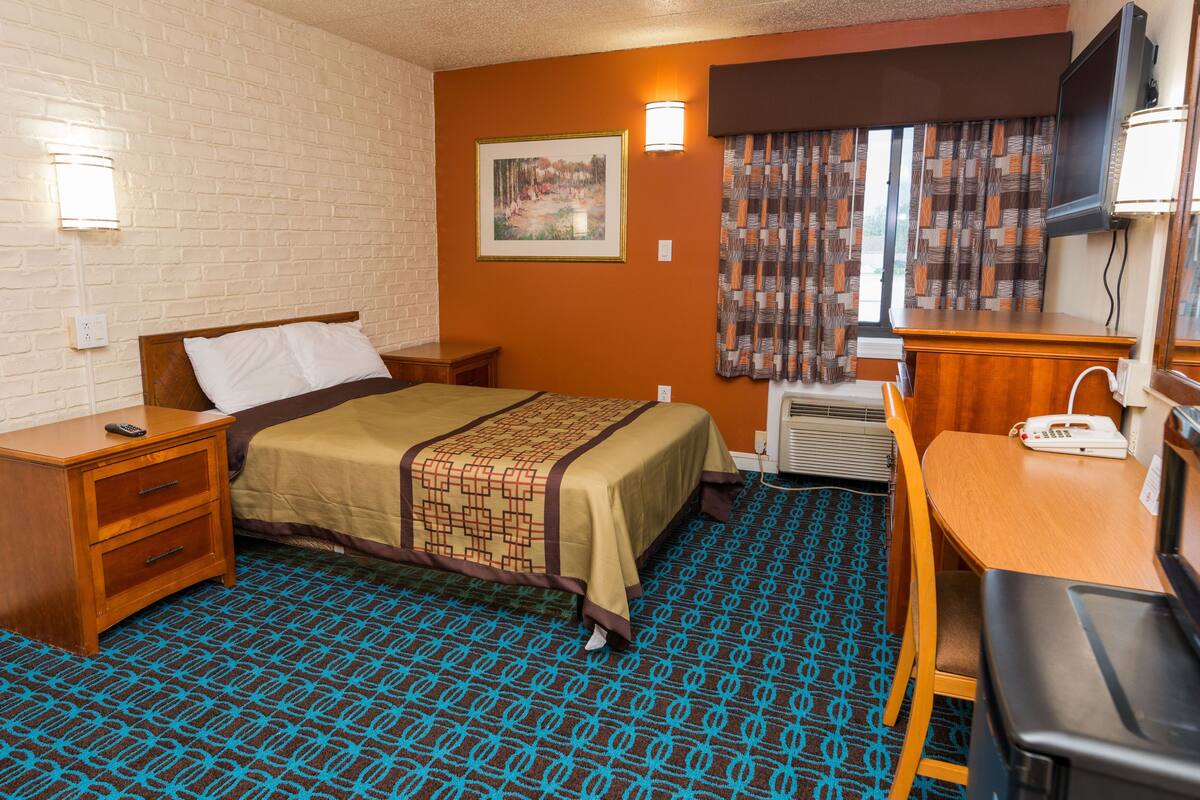 A hotel room with a bed, a desk, a chair, a TV, and a window with curtains.