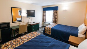 A hotel room with two beds, a desk with a computer, a microwave, a chair, a TV, and a window with curtains.