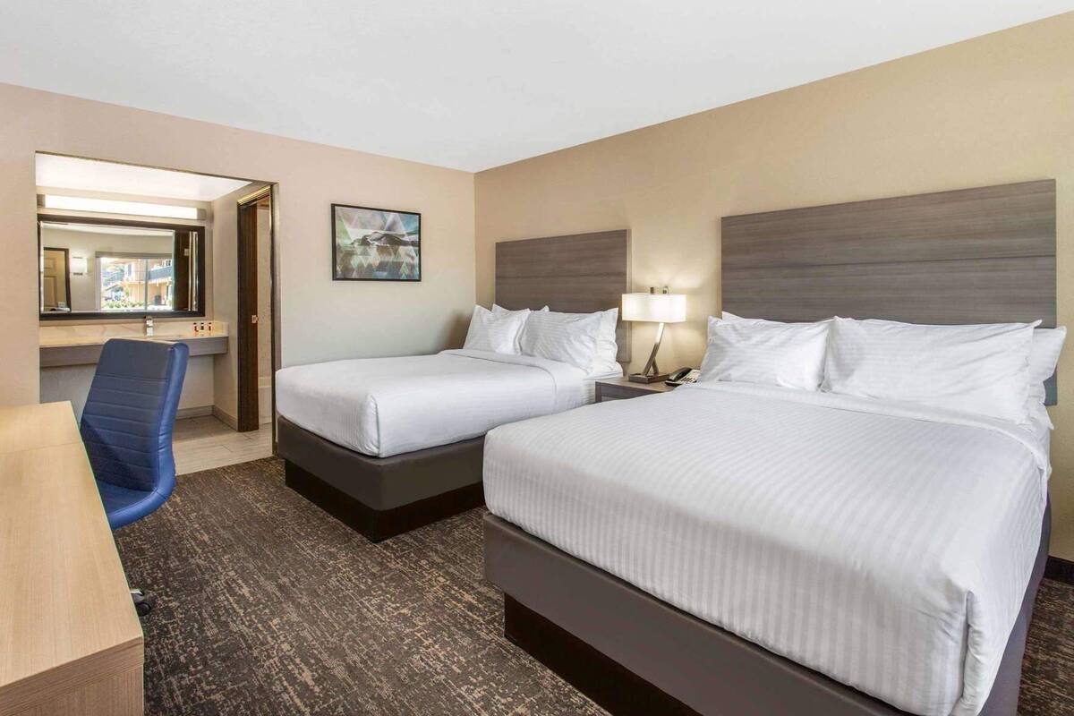 Une chambre d’hôtel avec deux lits, un bureau, une chaise, une lampe et un tableau au mur.