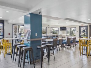 A modern restaurant with high tables and chairs, a blue pillar, and a clock on the wall. - Days Inn by Wyndham Merced / Yosemite Area (Merced)