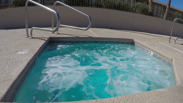 A rectangular hot tub with a metal ladder, surrounded by a concrete deck and palm trees. - Americas Best Value Inn Blythe (Blythe)