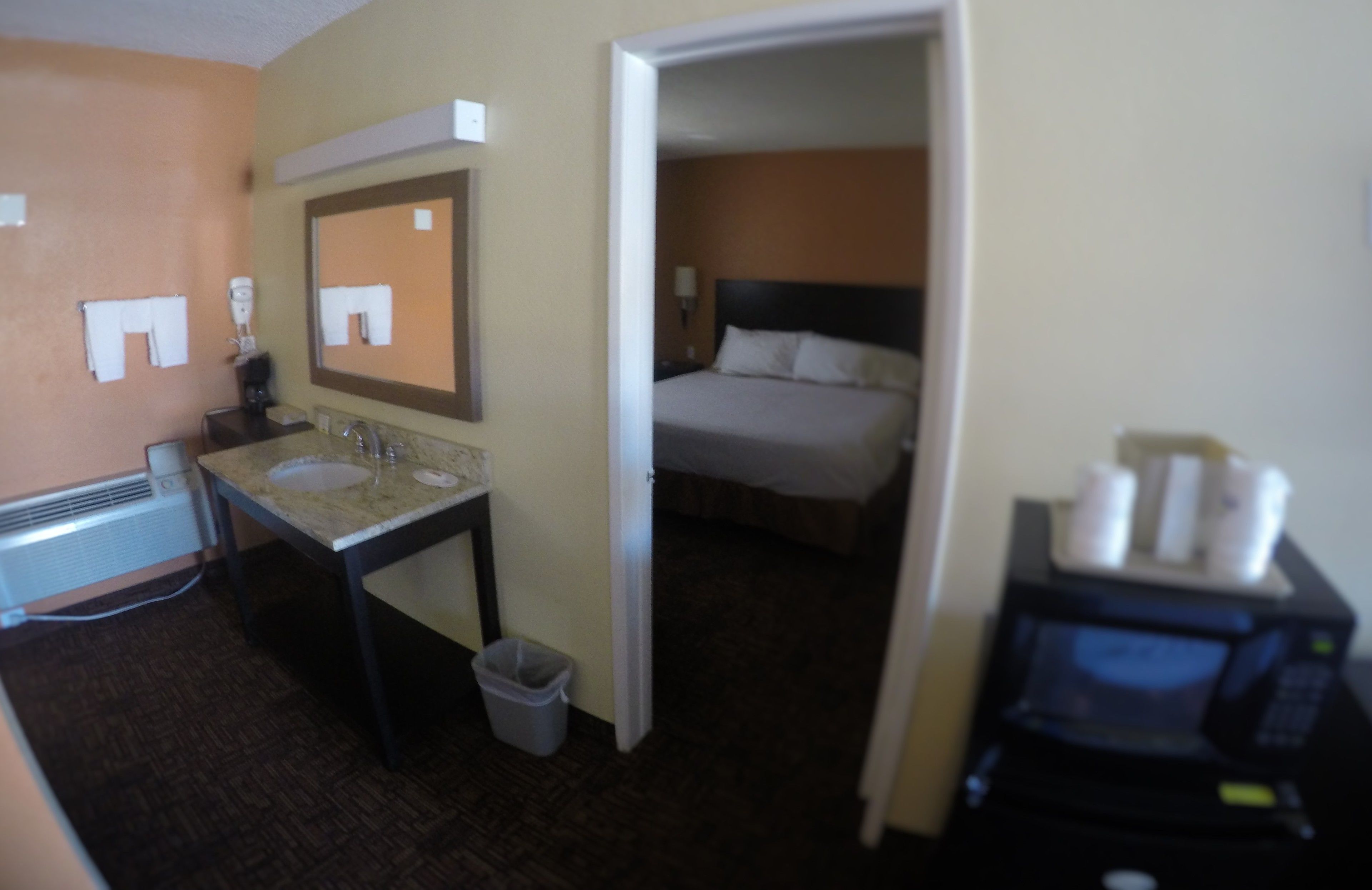 A hotel room with a bed, a bathroom with a sink and mirror, and a microwave.