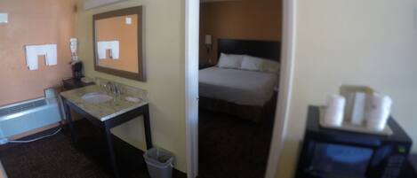 A hotel room with a bed, a bathroom with a sink and mirror, and a microwave.