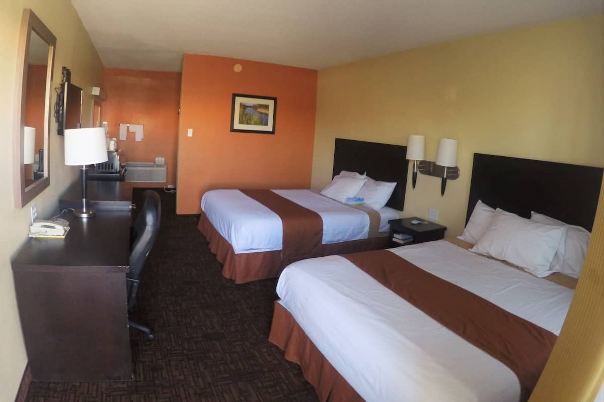 A hotel room with two beds, a desk, a chair, a lamp, and a painting on the wall.
