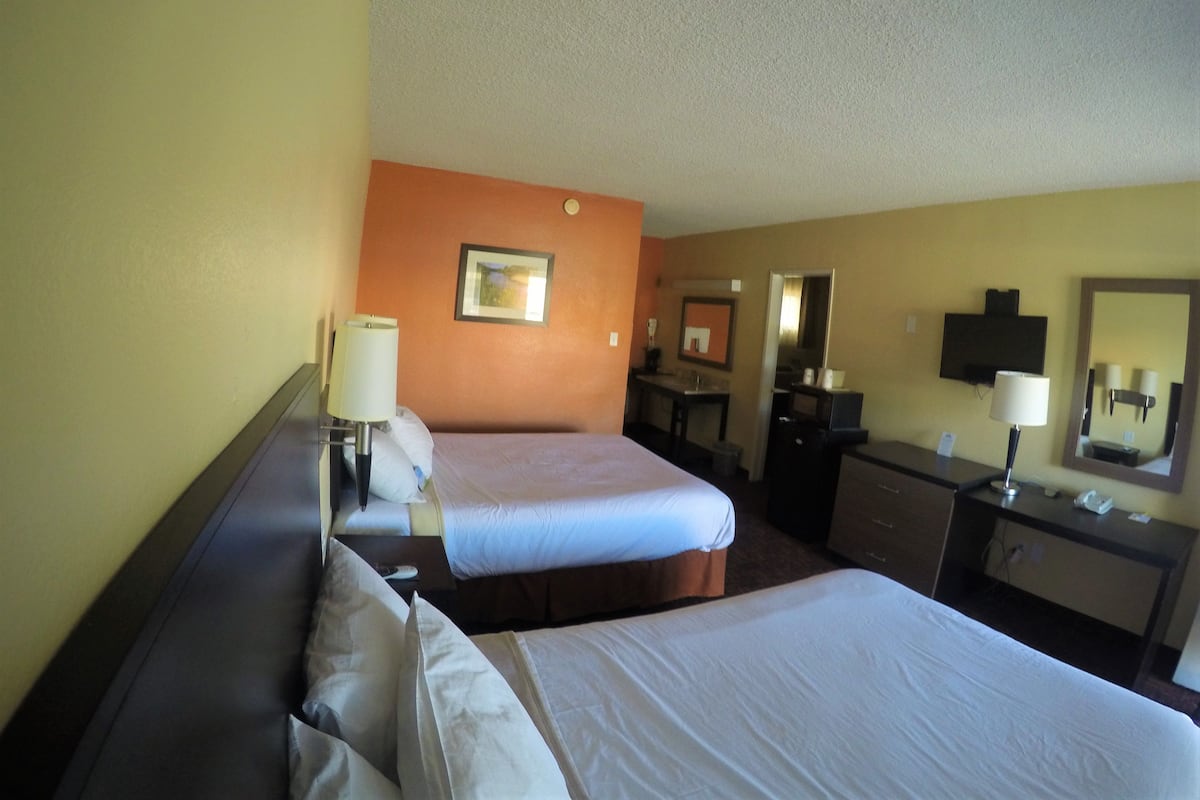 A hotel room with two beds, a desk, a dresser, a mirror, and a TV.