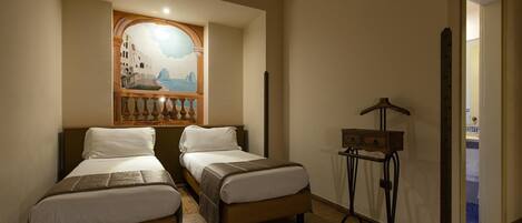 Een hotelkamer met twee bedden, een houten vloer, een klein tafeltje met een lamp en een muurschildering.