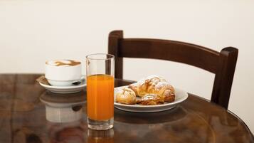 Ein Esstisch mit einem Glas Orangensaft, einer Tellerr voller Croissants und einer Tasse Kaffee.
